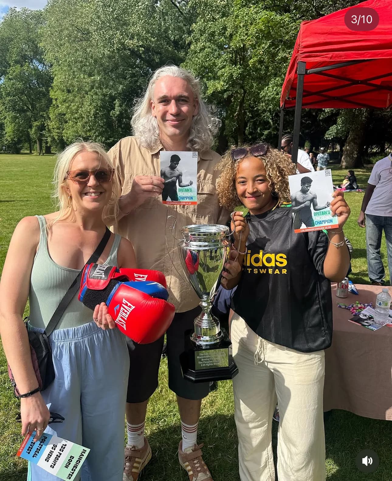 Campaign supporters at a park stall hold Len Johnson Campaign leaflets and boxing gloves beside the Cup