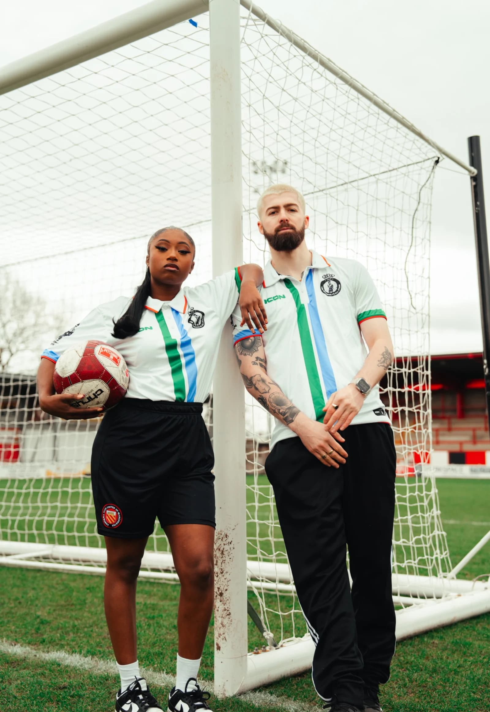 Two players pose by the goalpost, one holding the match ball