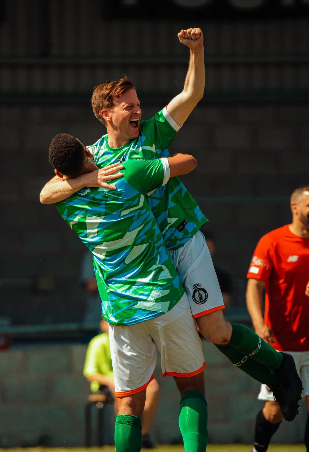 Two players celebrate a goal together on the pitch, one lifted off the ground