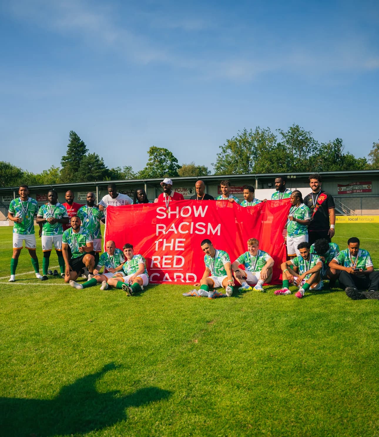 Players from both teams sit and stand together holding a Show Racism the Red Card banner after the match