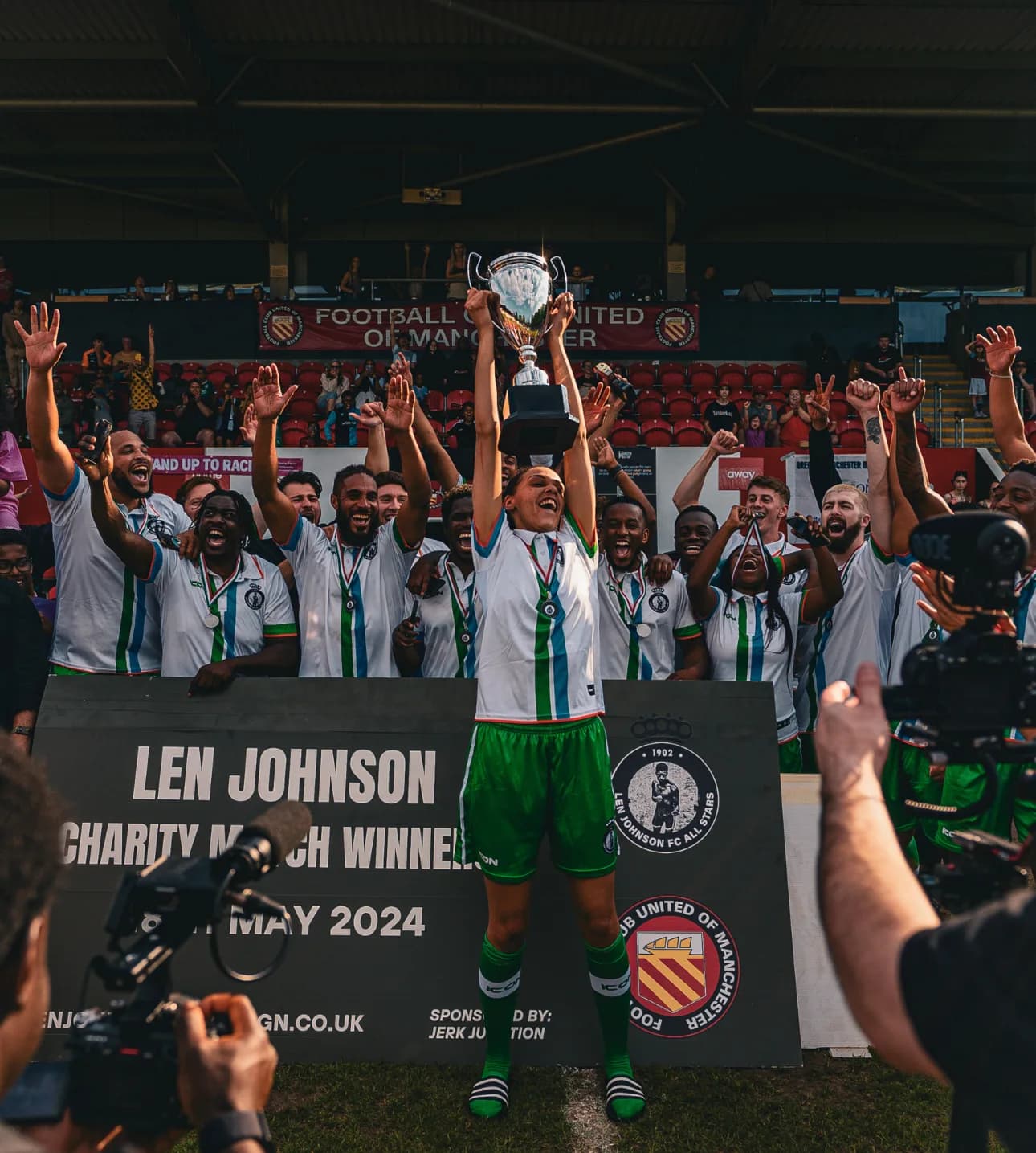 The Len Johnson All Stars lift the trophy in front of a board reading Len Johnson Charity Match Winners, 4 May 2024