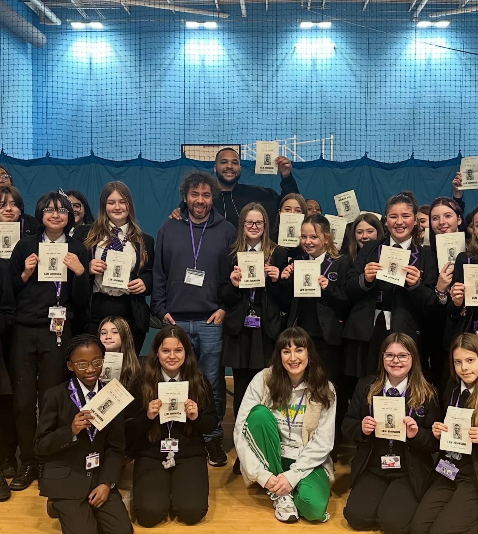 A school group poses together holding printed Len Johnson name cards from the workshop