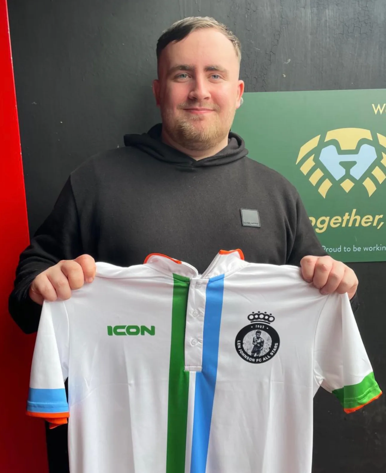 Darts player Luke Littler holds a Len Johnson FC All Stars shirt