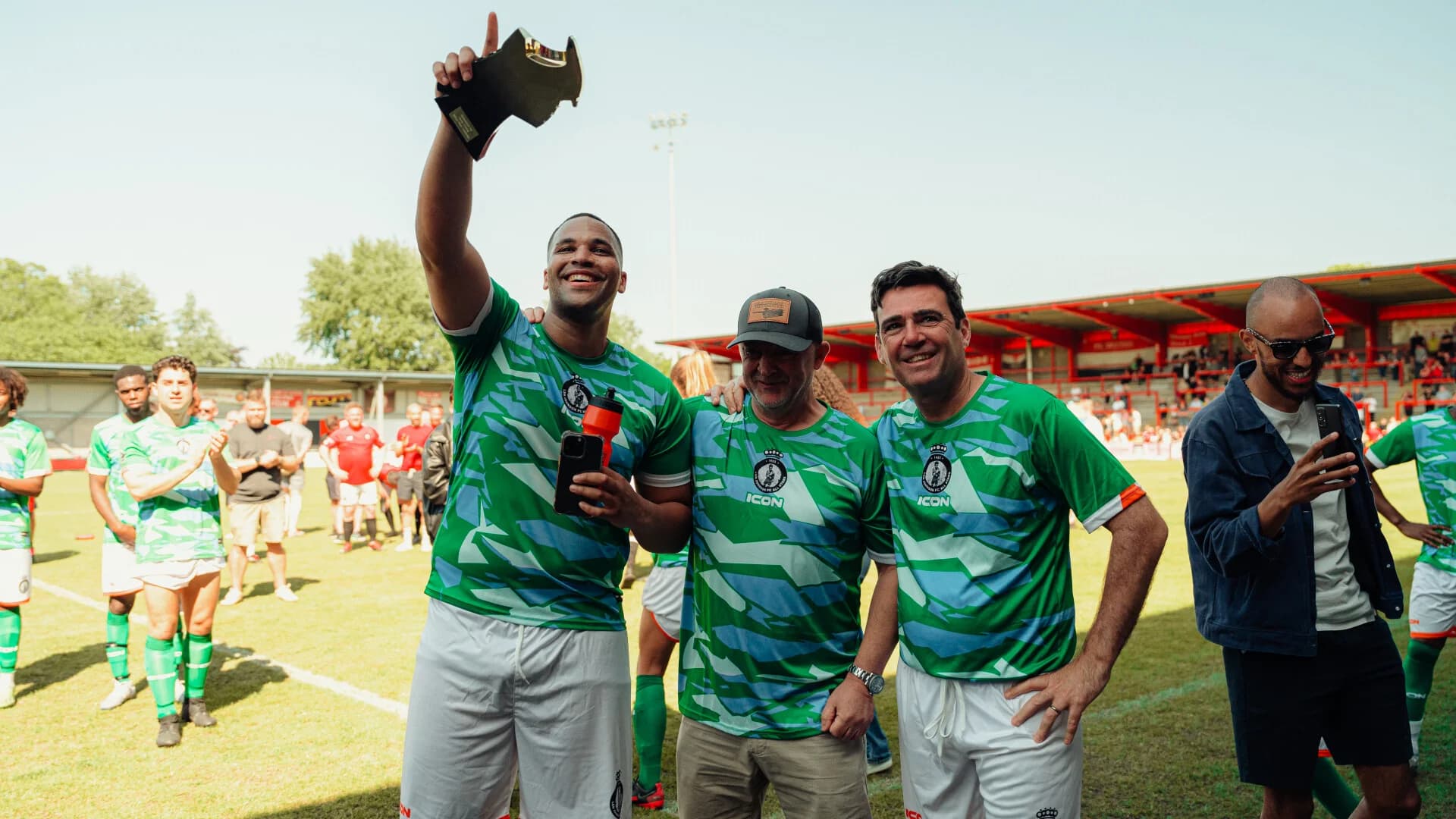 Three men pitchside with the charity match trophy