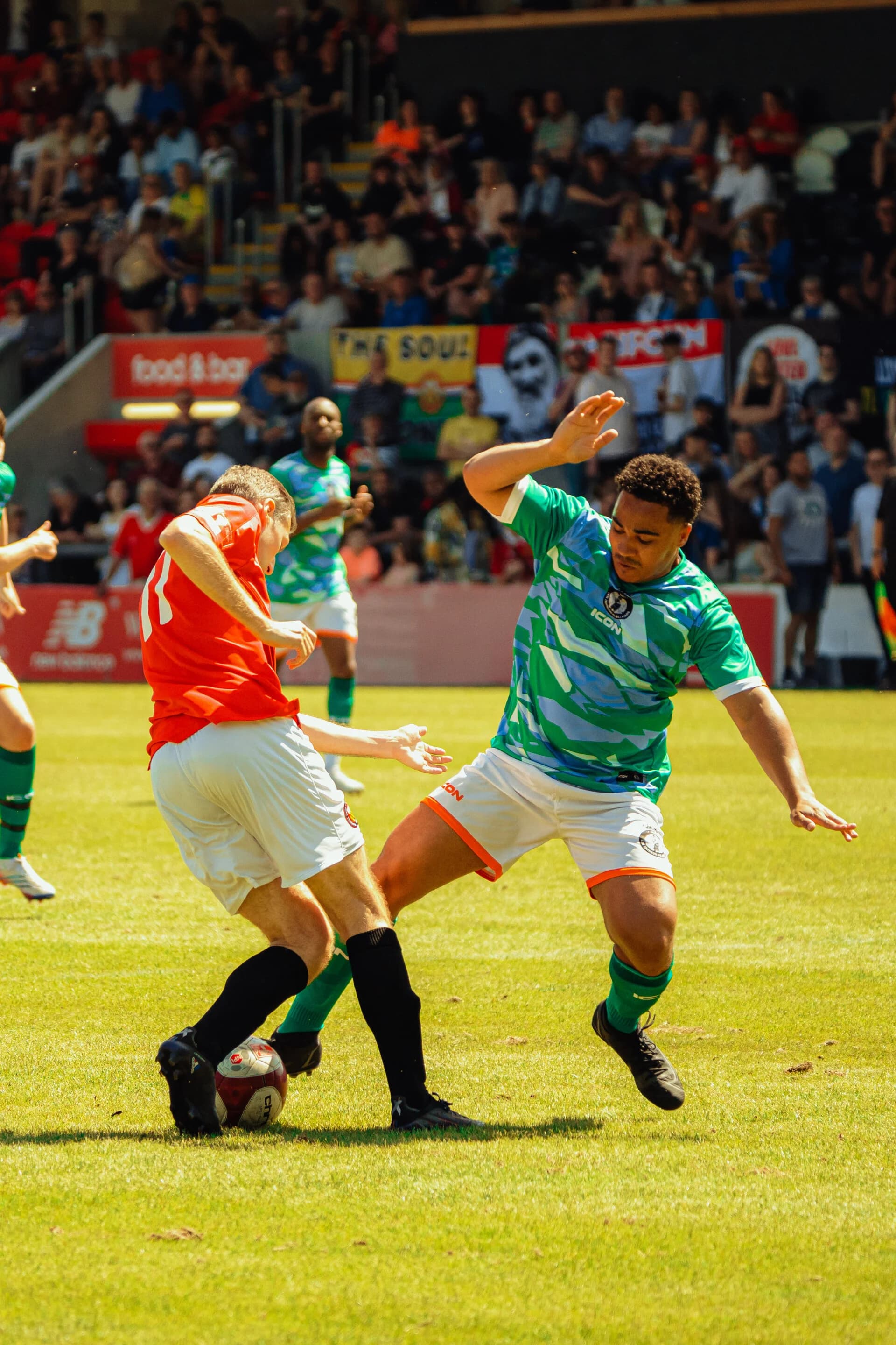 A player in red wins the ball off a player in green during the charity match