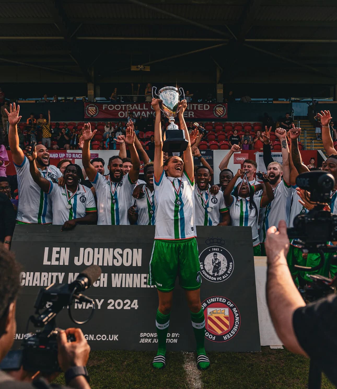 The winning team celebrate with the Len Johnson Cup under a banner reading "Len Johnson Charity Match Winners, 4th May"